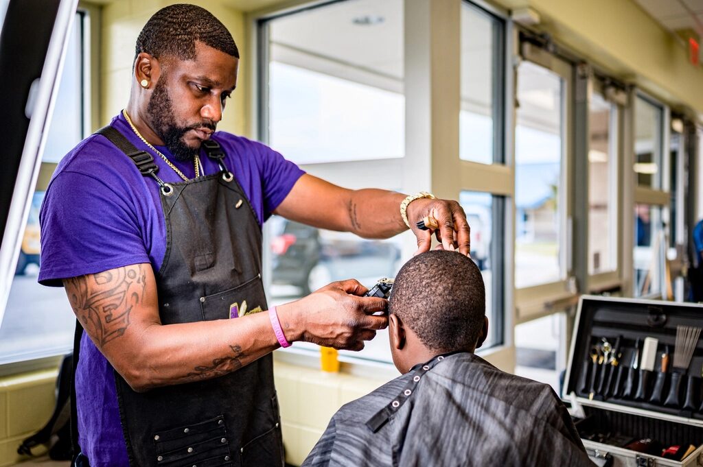 Barber working clippers on a client by the shop window