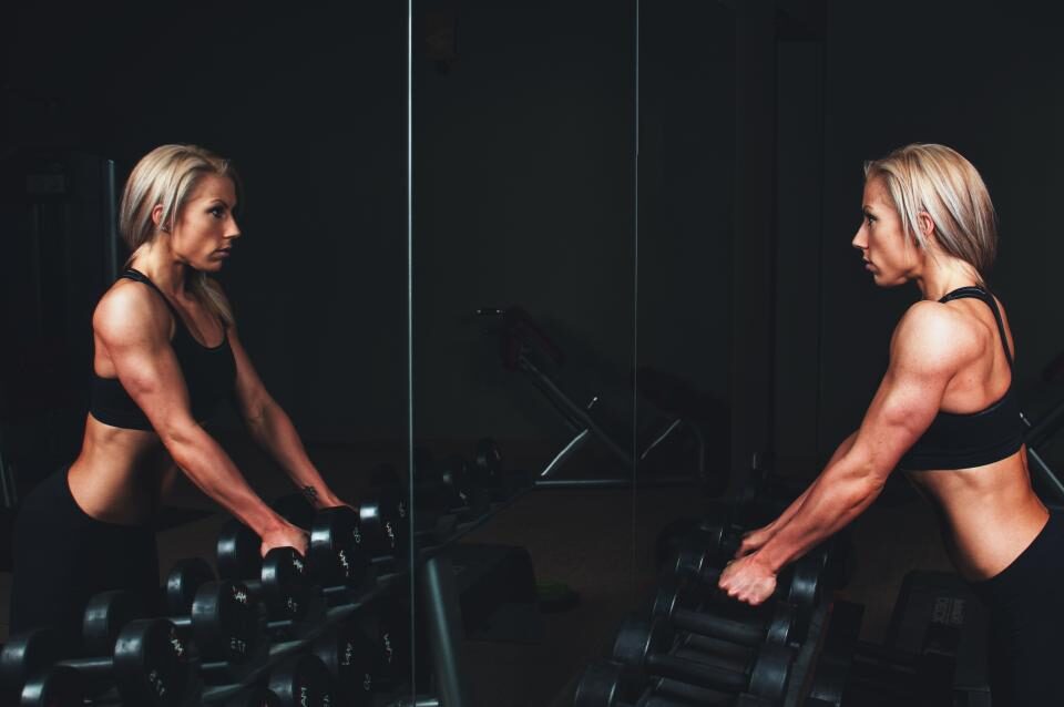 Athlete reaching for dumbbells at a mirrored rack