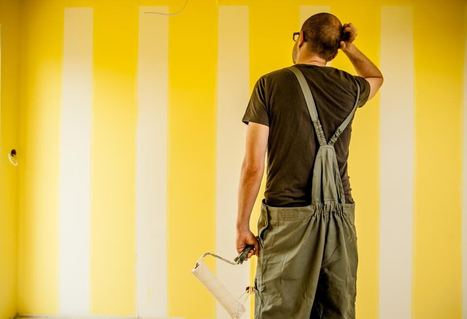 Painter with a roller studying a striped yellow wall