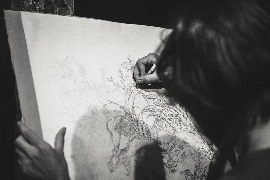 Artist sketching a detailed floral design on a large sheet of paper
